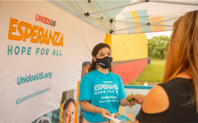Latina woman in a mask handing out information at a mobile vaccination clinic.