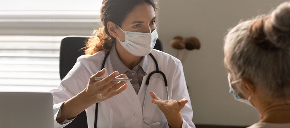 Female doctor consult old patient in facemask.