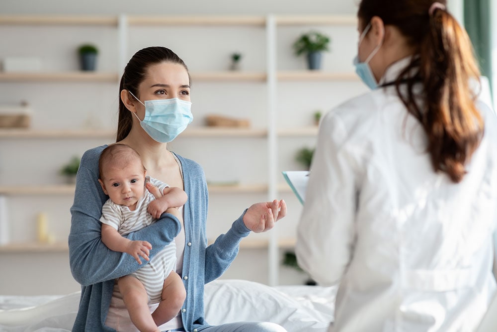 Doctor in protective mask talking to a mother with newborn baby.