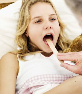 close-up of a male doctor putting a tongue depressor into a girl's mouth.