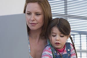 Madre sentada con su hija frente a una computadora portátil.