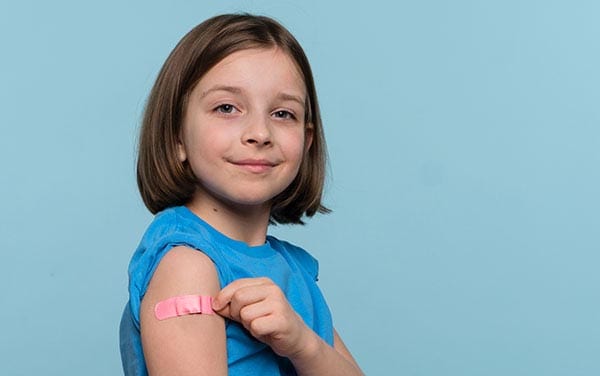 Little girl pointing finger at adhesive bandage on her arm after being vaccinated