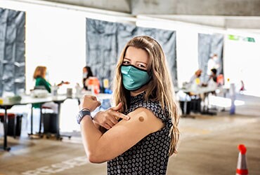 Woman in a mask pointing to her arm where she was vaccinated.