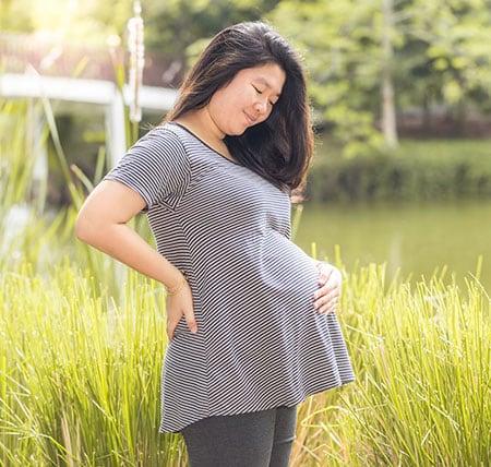 Pregnant woman standing outside holding her belly.