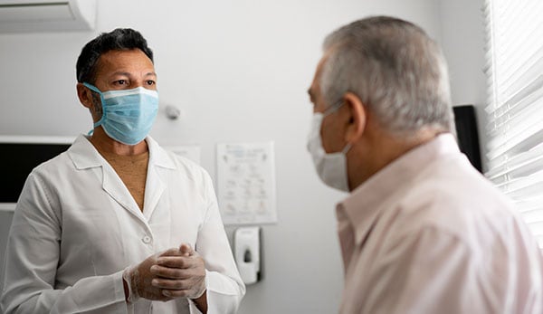 Masked doctor talking with older male patient