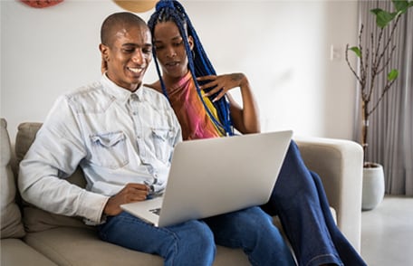Image of a smiling couple viewing a computer screen while sitting on a couch