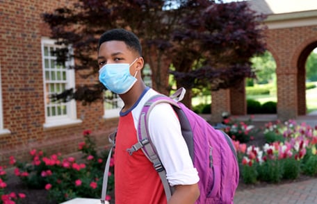 Teen student with backpack and mask on campus