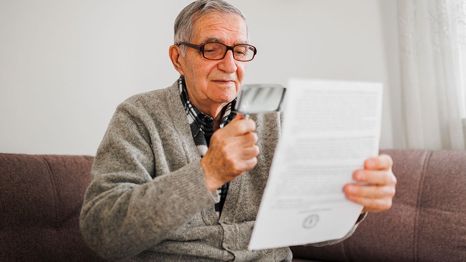 elderly person with looks at document with magnifying glass