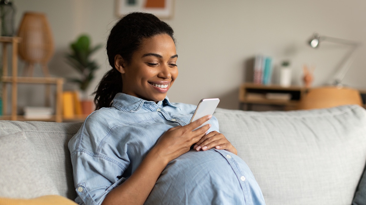 Pregnant woman sitting on a sofa, smiling at her cell phone