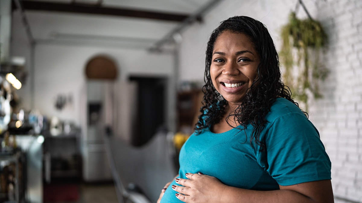 Pregnant woman in her home and smiling at the camera.