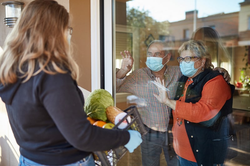 woman looking through window at two elderly people wearing face coverings