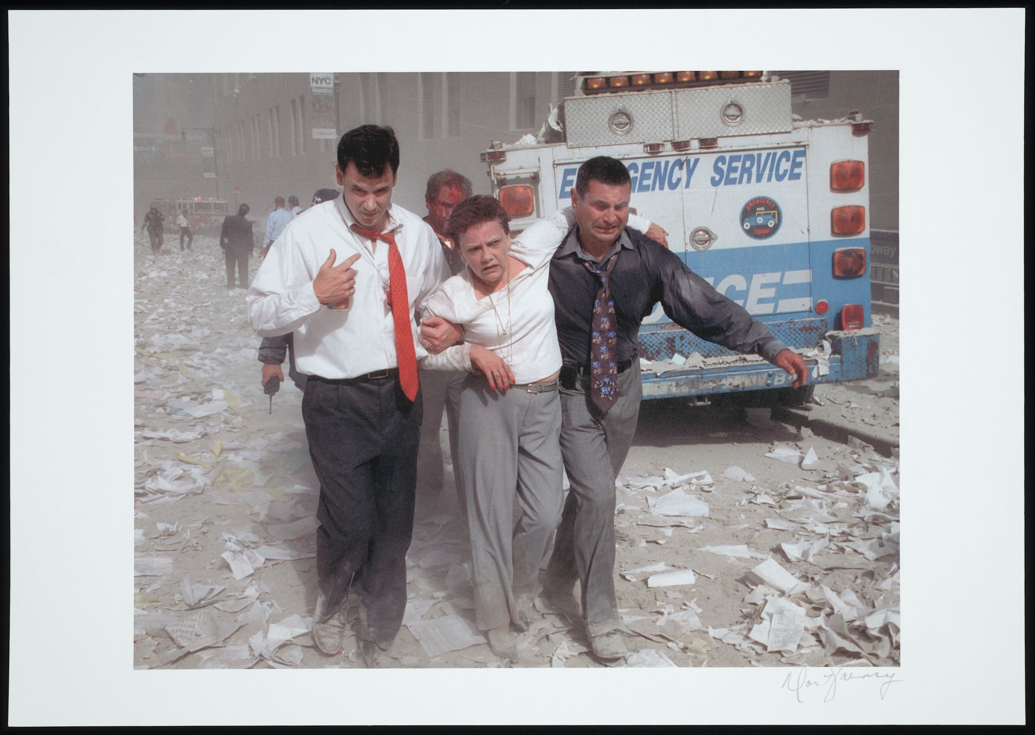 Two men carry an injured woman down a street littered with paper, ashes, and dust from the Twin Towers’ collapse. 