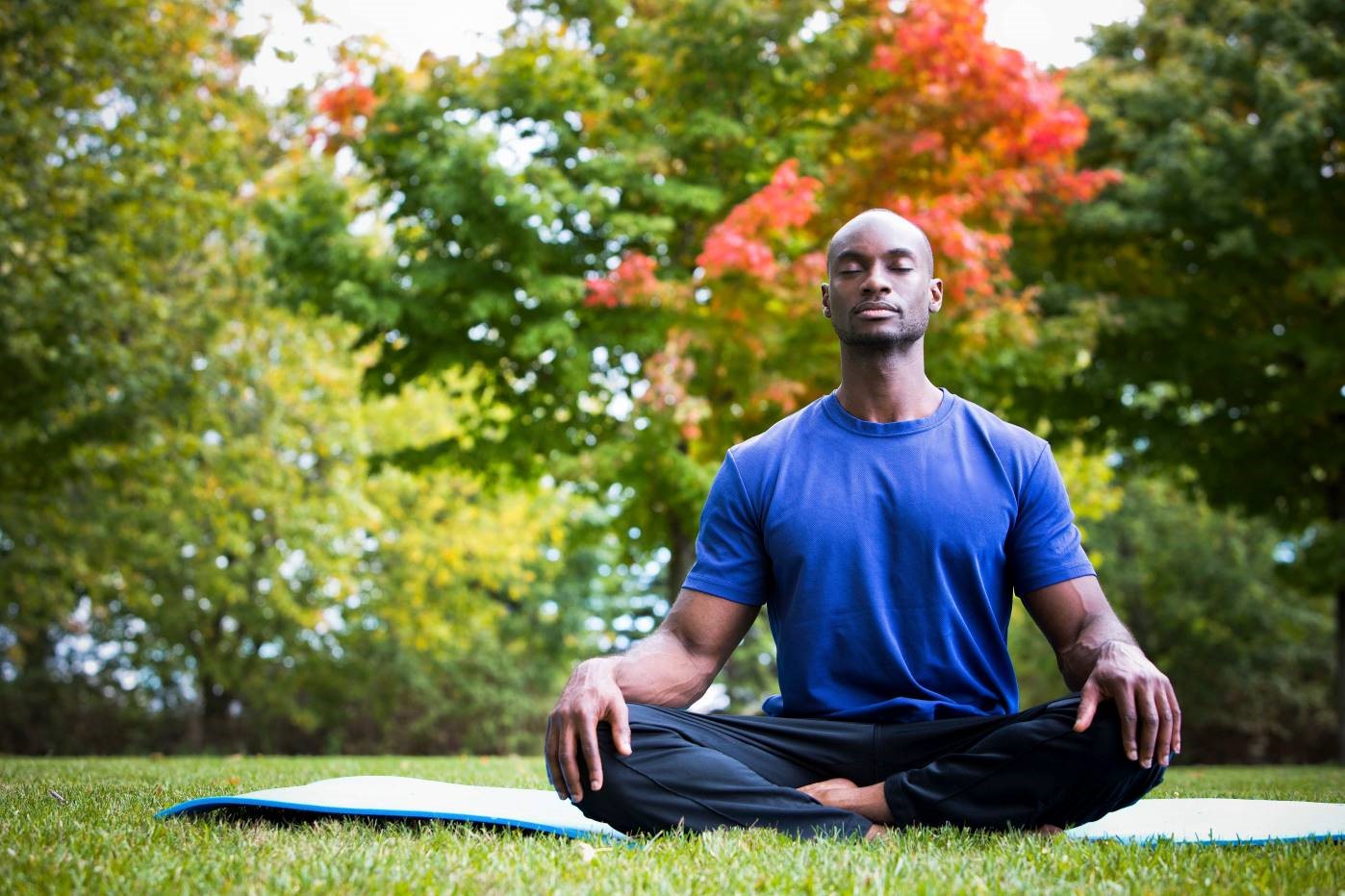 Man meditating on a yoga mat in a grassy field.