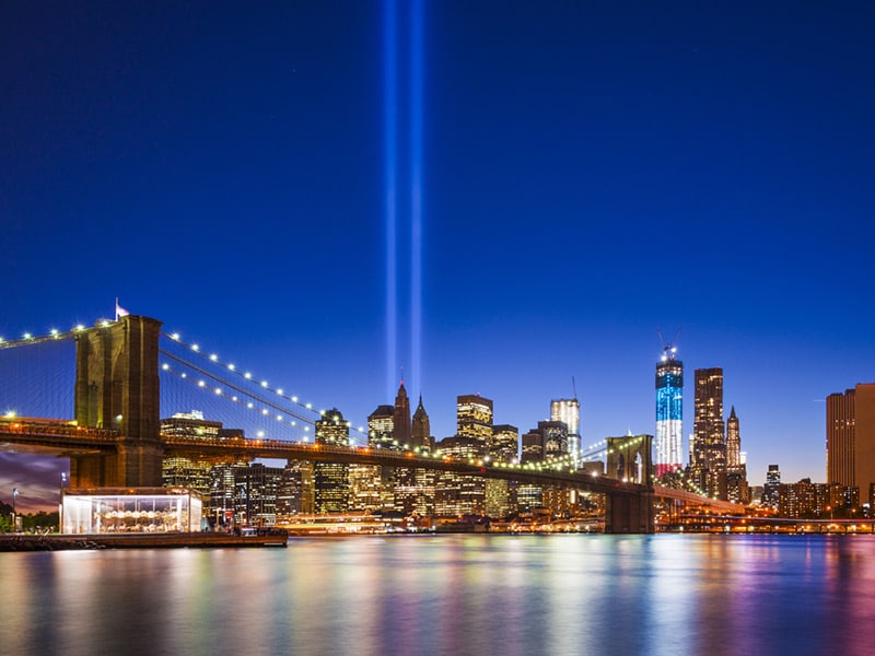 Photo of the WTC Memorial towers of light at twilight, seen from the surface of the East River, opposite the Brooklyn Bridge