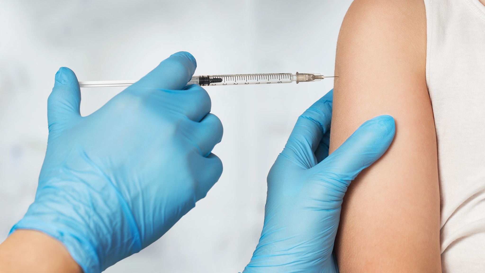 Gloved hands inserting a vaccine syringe into an arm.
