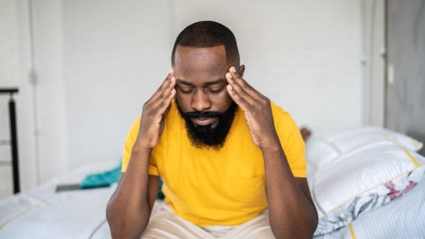 Man holding his head while sitting on the edge of a bed.