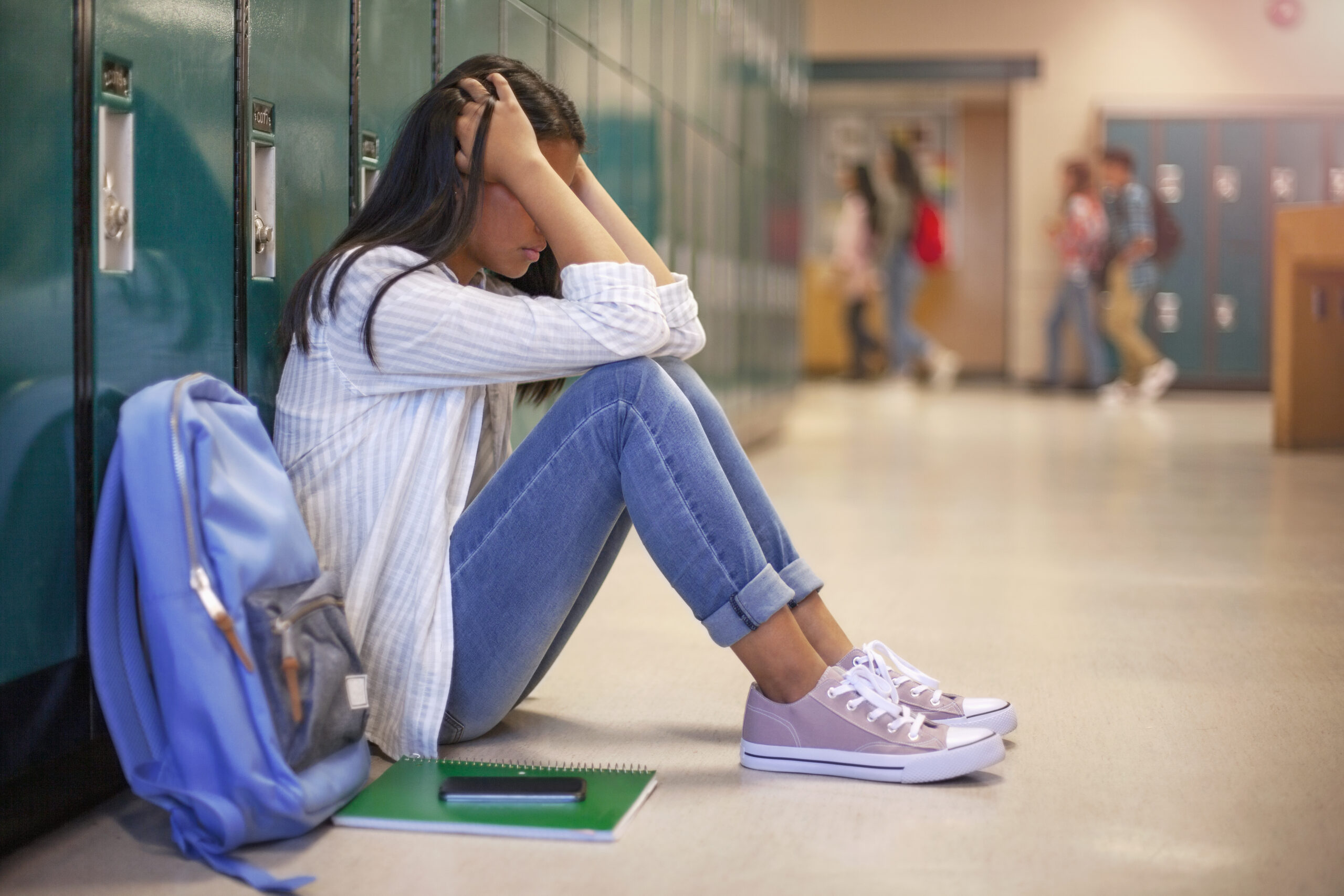 A high school student sitting by herself in front of lockers.