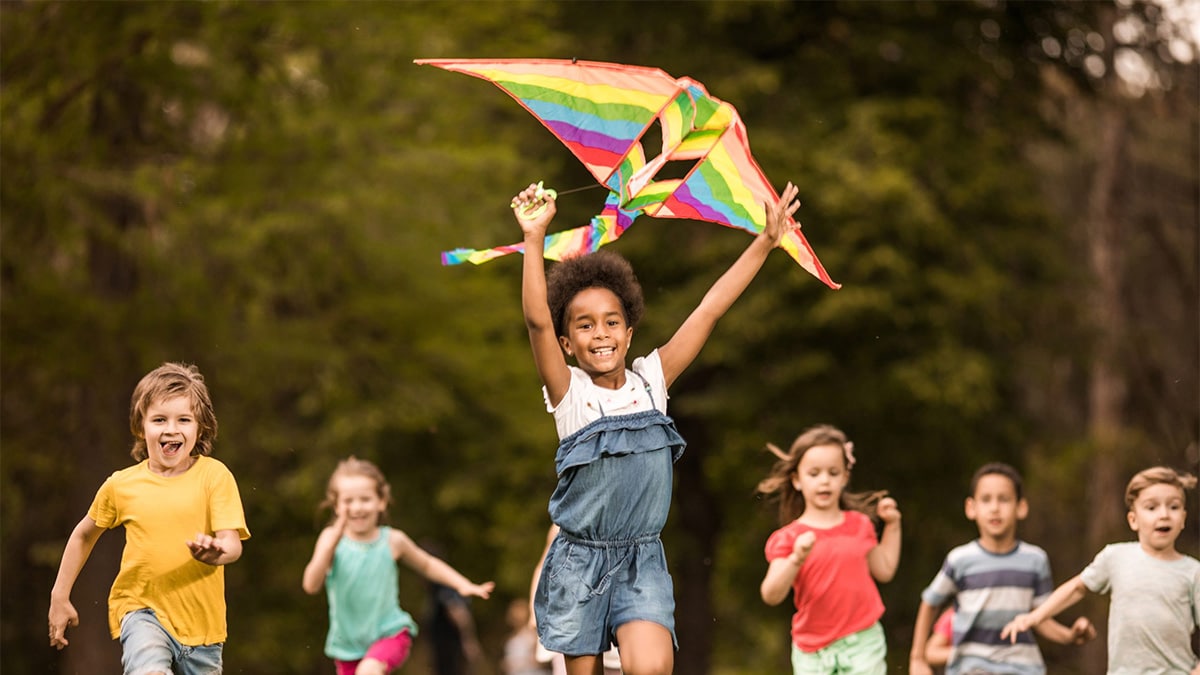 Group of young children running outside while playing with a kite.