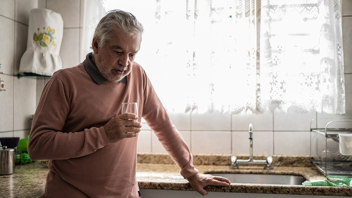 A man standing by the sick in his kitchen while drinking a glass of water