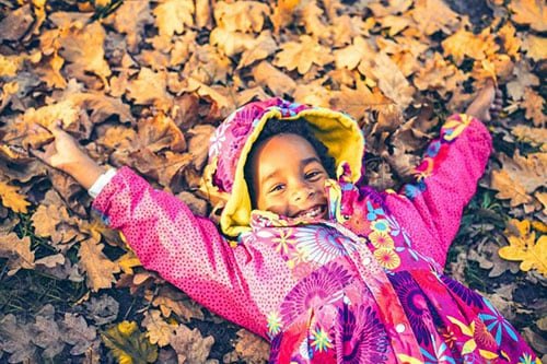 young girl smiles as she plays in autumn leaves
