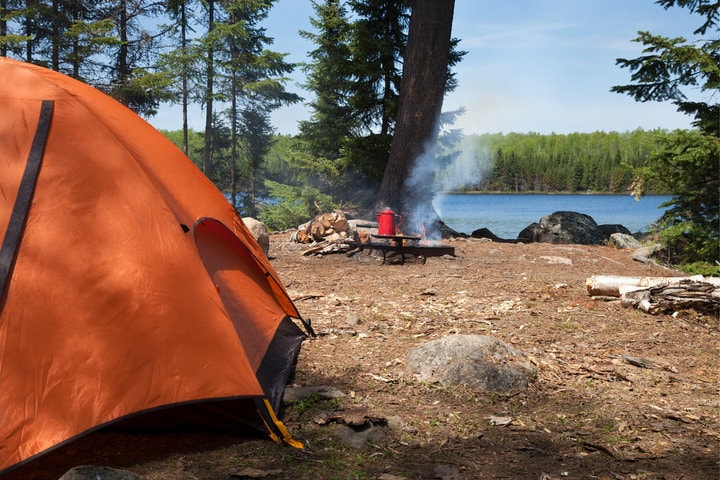 Campsite by lake with orange tent.