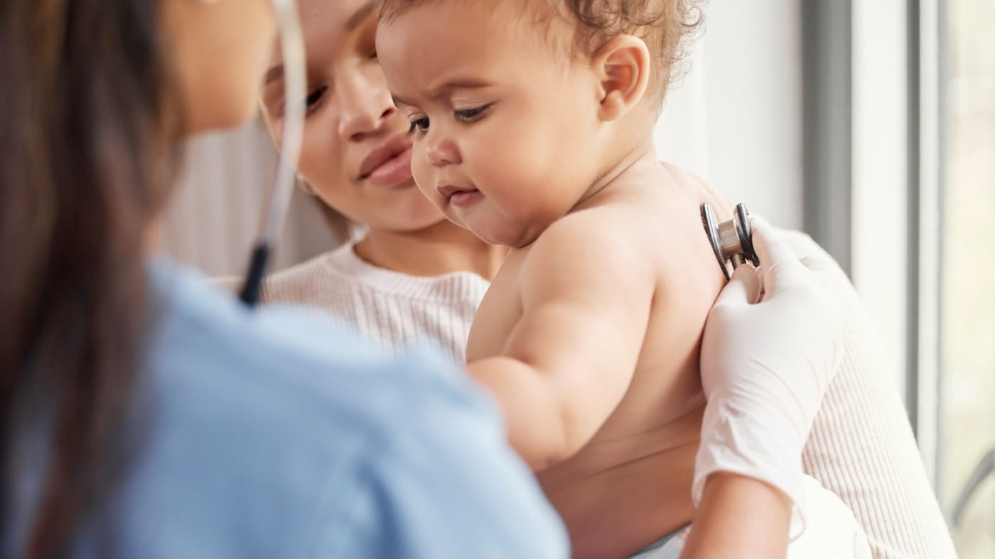 Public health nurse places stethoscope on baby's back