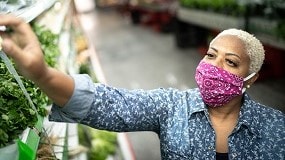 Woman wearing a mask and buying vegetables at a grocery store.