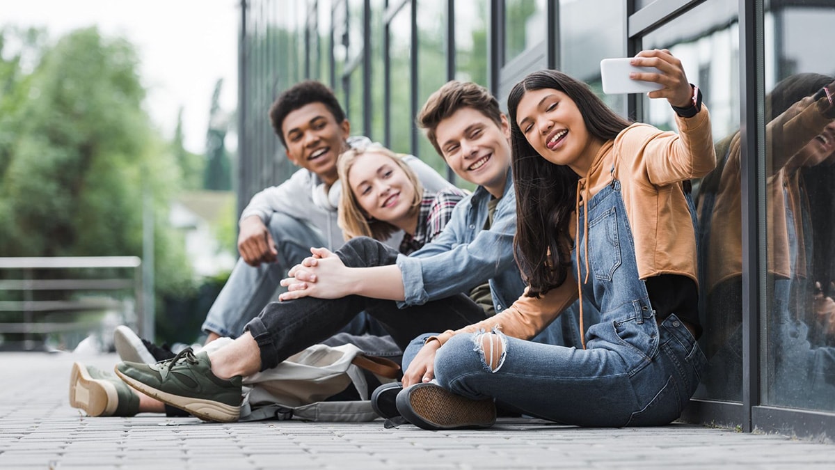 A group of teens smiling, sitting and taking selfie with smartphone