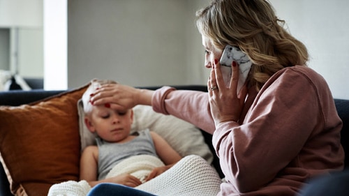 Mother checking to see if ill son feels warm while on the phone